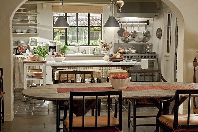 Cozy kitchen with arched doorway, wooden table, stools, hanging pots, and bright window over the sink