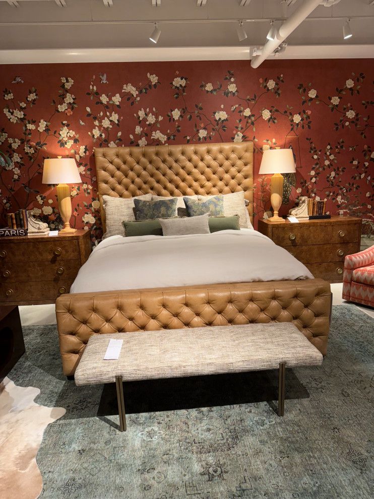 Tufted bed with white bedding, bench, and matching lamps against red floral wallpaper in a bedroom showroom