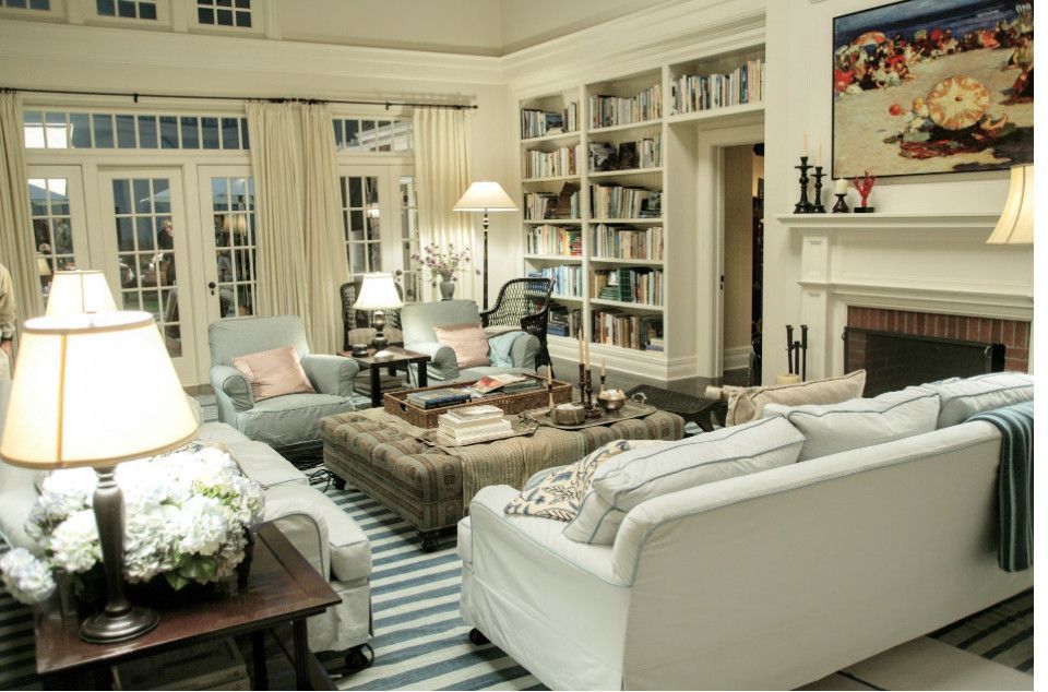 Cozy living room with white sofas, striped rug, bookshelves, fireplace, and large windows