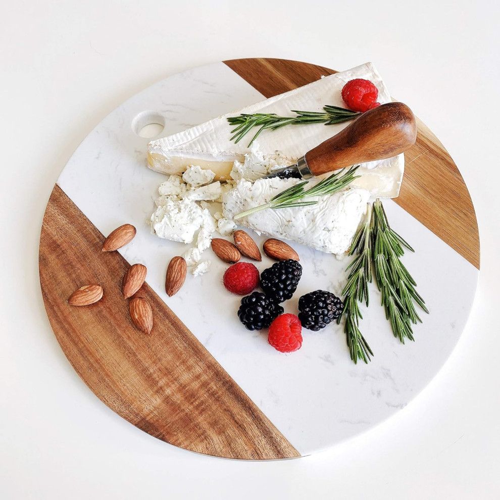 Brie cheese with berries, almonds, rosemary, and a knife on a round white and wood serving board