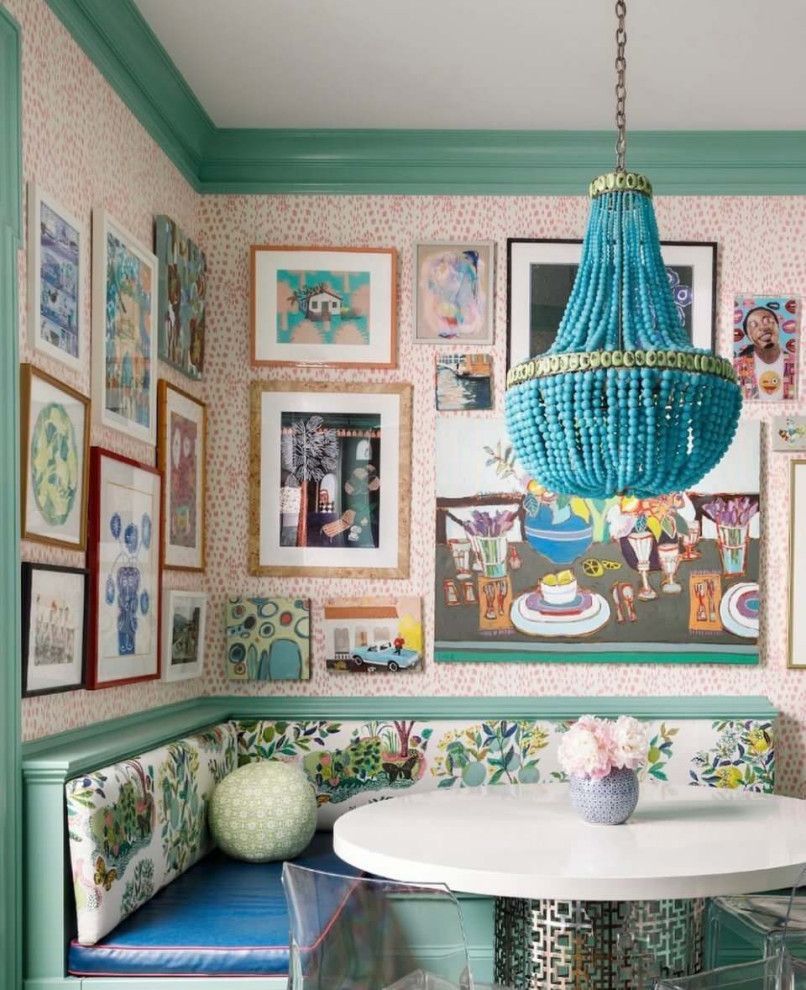 Colorful gallery wall in a cozy nook with a teal chandelier, white table, and bench seating
