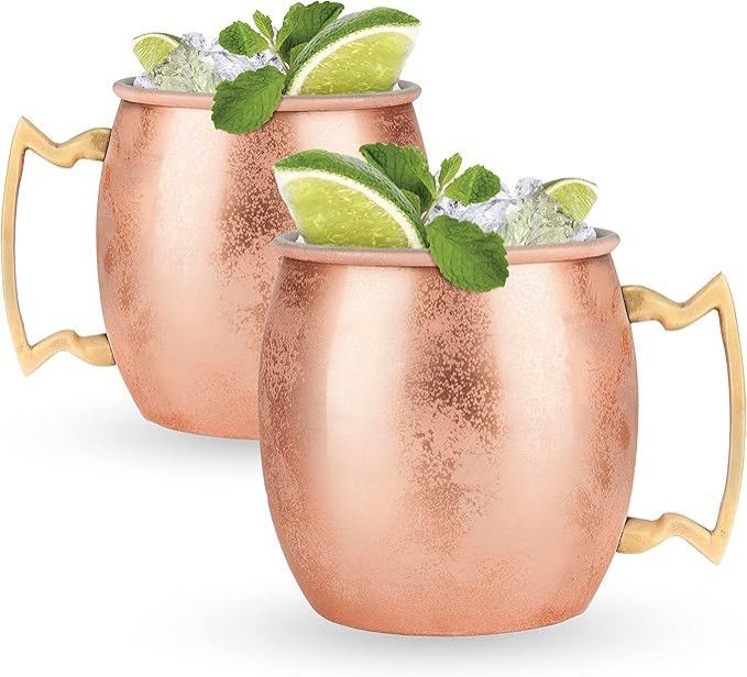 Two copper Moscow mule mugs with lime wedges and mint leaves on a white background