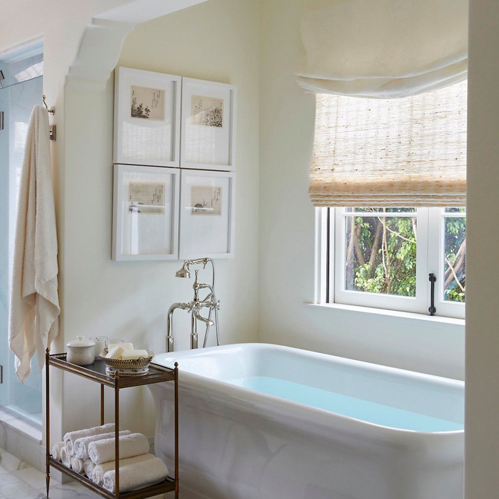 Bright bathroom with a white soaking tub, brass fixtures, window shade, and framed wall art.