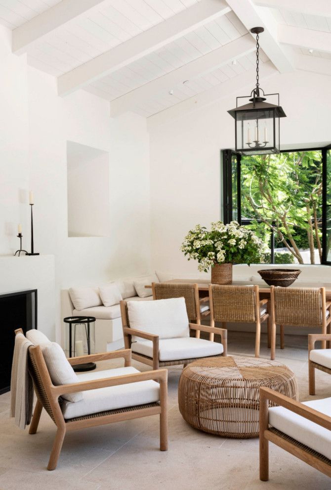 Bright white living room with wooden chairs, woven ottoman, and open window to greenery