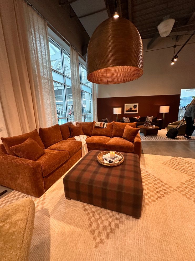 Cozy living room with orange sectional sofa, plaid ottoman, and large pendant light beside tall windows