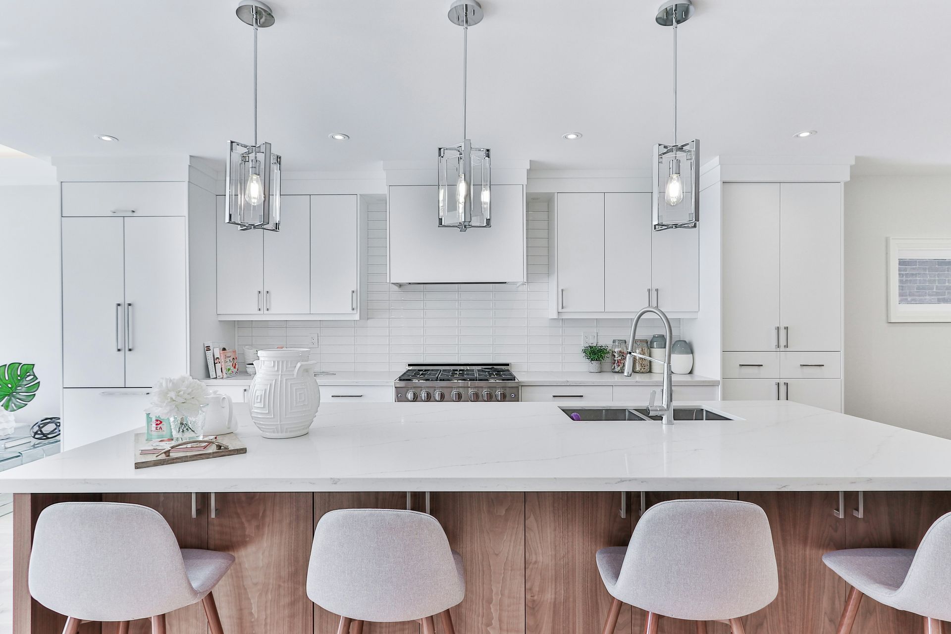 Bright white modern kitchen with island, pendant lights, barstools, and stainless steel range