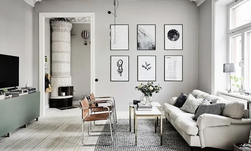 Bright minimalist living room with gray sofa, glass coffee table, framed wall art, and large window light