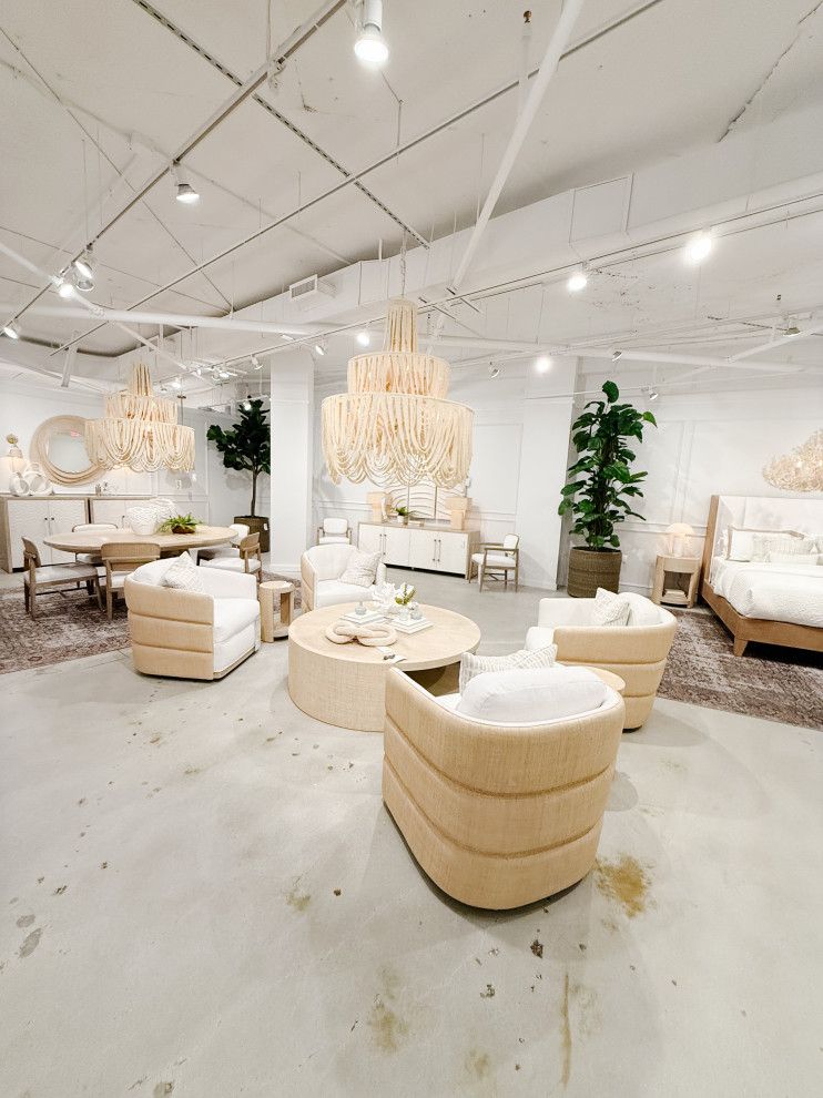 Elegant white lounge showroom with cream seating, round tables, chandeliers, and tall plants