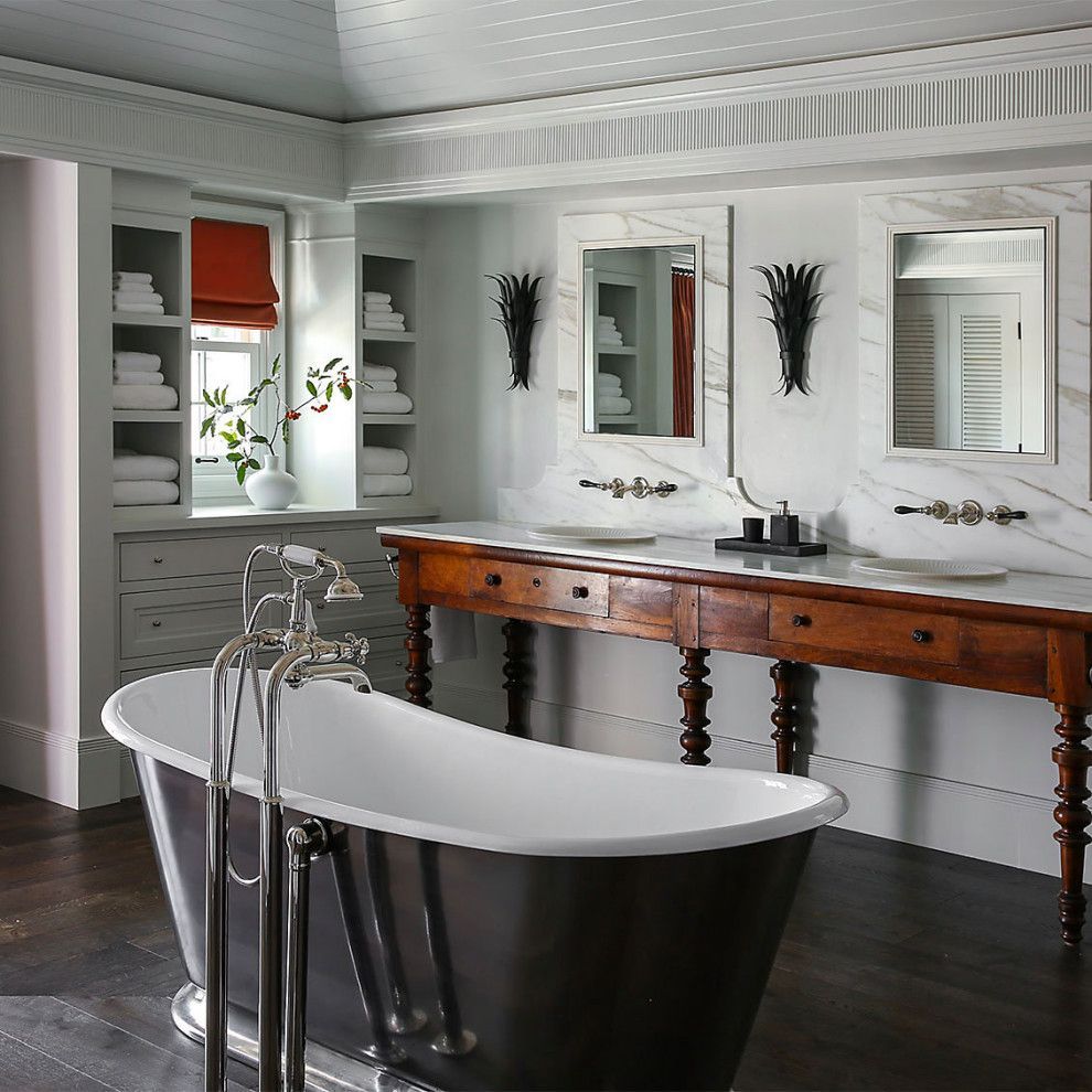 Modern bathroom with a freestanding tub, double vanity, mirrors, and white cabinets with dark wood flooring