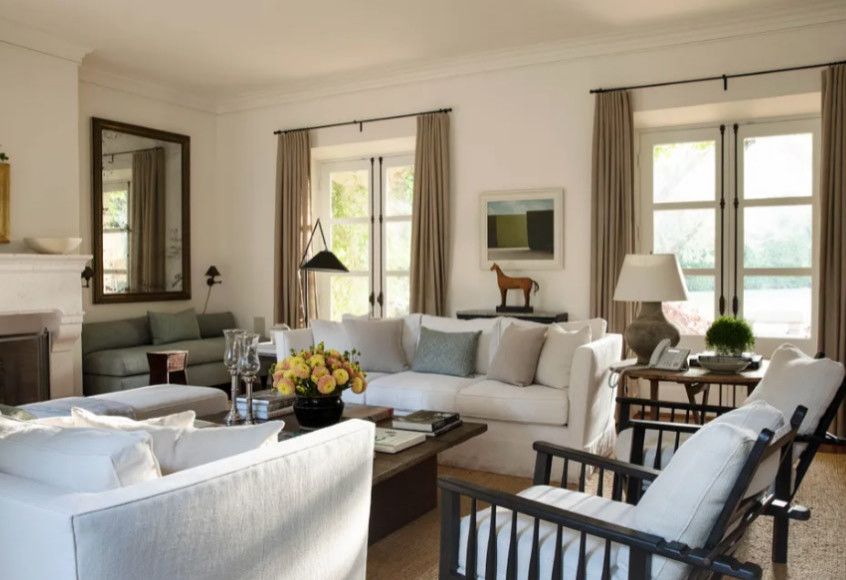 Bright living room with white sofas, coffee table, lamps, and large windows