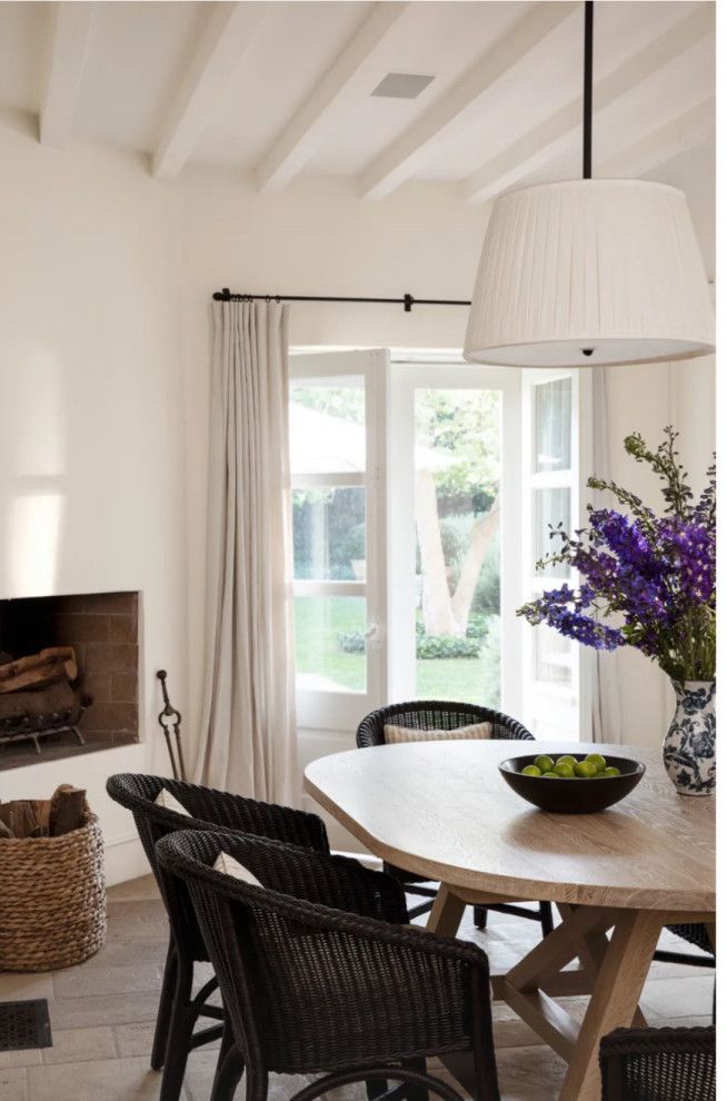 Bright dining room with round table, wicker chairs, pendant lamp, and vase of purple flowers by the window