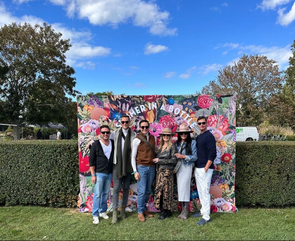Six people posing in front of a colorful graffiti backdrop outdoors on a sunny day.