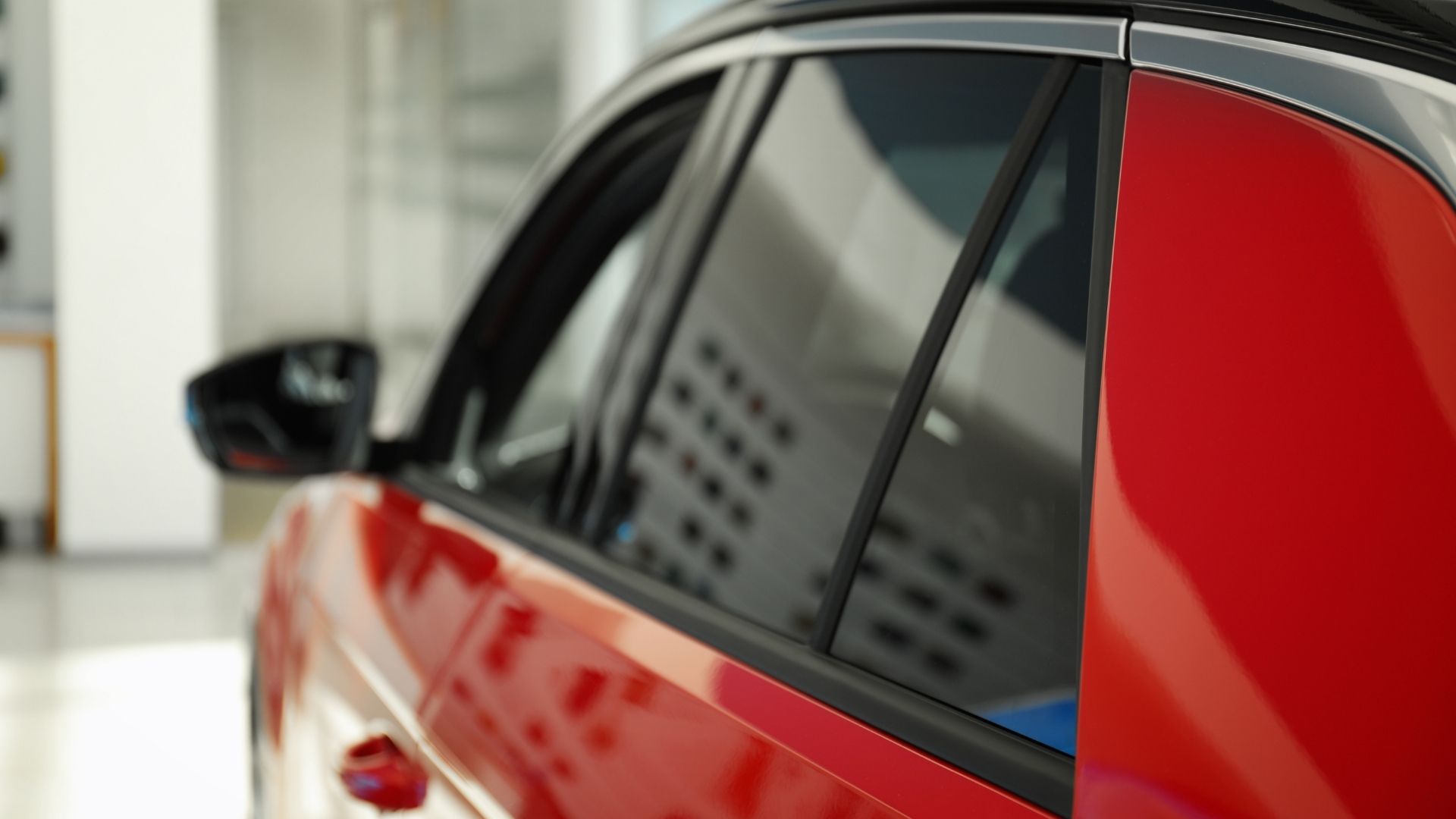 Close-up of a red car’s side windows and black trim in a bright showroom