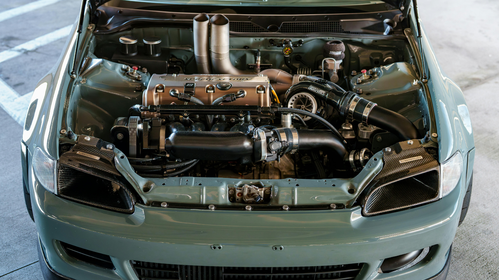 Front view of a silver sports car with its hood open, showing a customized engine bay.