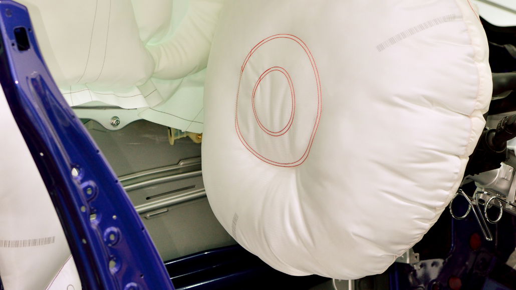 White inflatable airbag inside a car with blue door frame and white interior upholstery