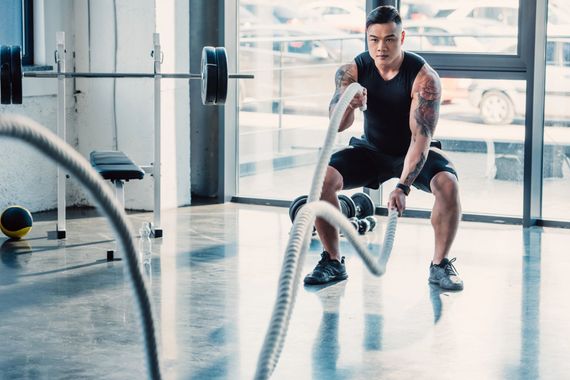 Persona che si allena con le corde da battaglia in una palestra luminosa con grandi finestre.