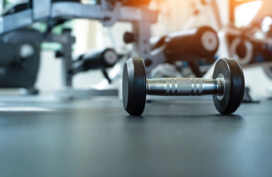 Manubrio sul pavimento della palestra con attrezzi da allenamento sfocati sullo sfondo.