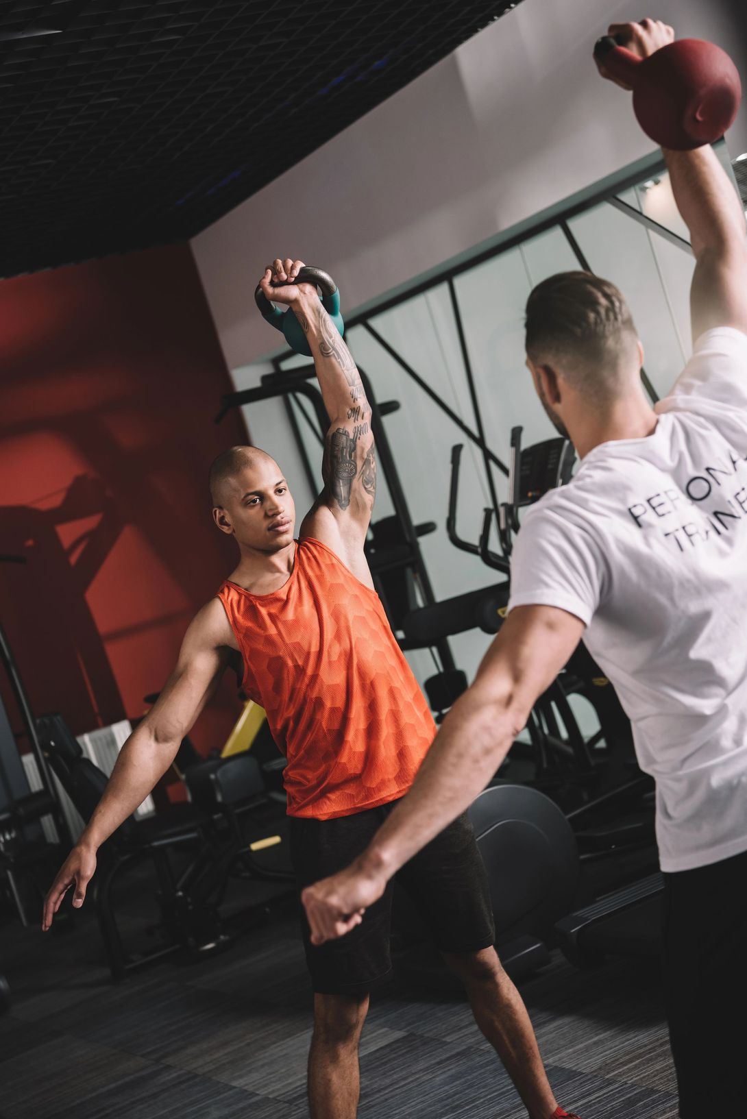 Persone che si allenano in palestra, sollevando kettlebell con un braccio alzato.
