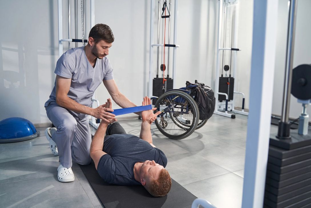 Fisioterapista assiste un paziente nell'esecuzione di esercizi per le gambe nella palestra di una clinica.
