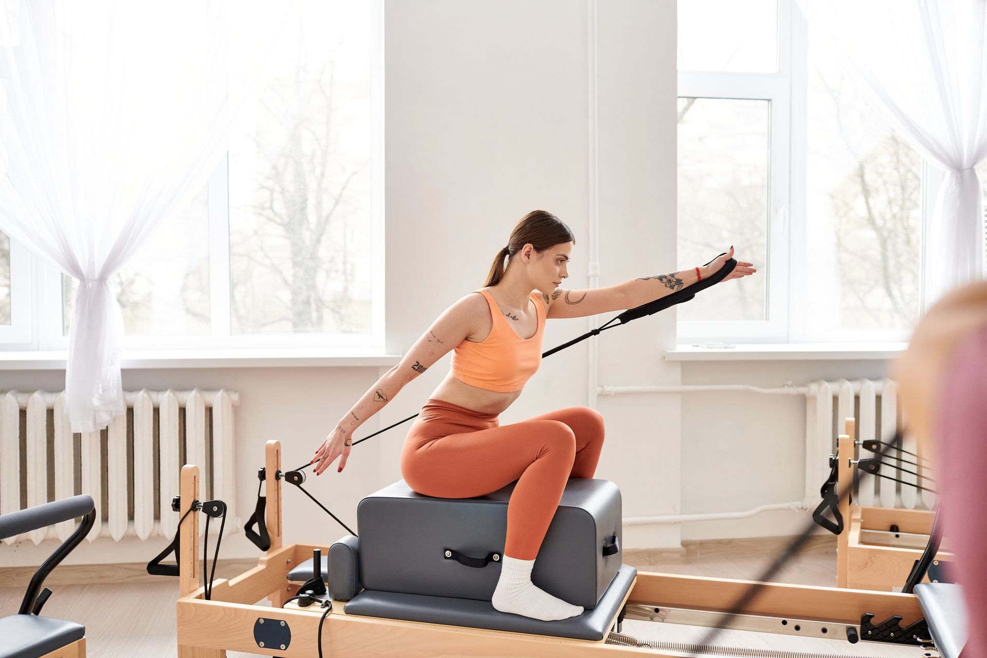 Una donna esegue un esercizio di Pilates su una macchina reformer in uno studio luminoso.