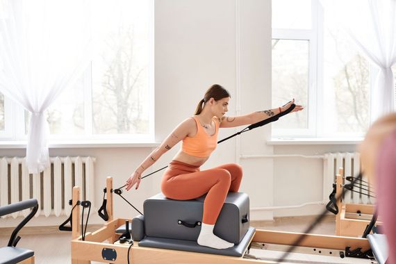 Una donna esegue un esercizio di Pilates su una macchina reformer in uno studio luminoso.