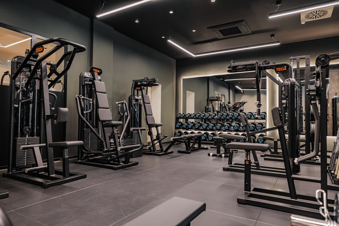 Due persone che fanno step-up in una palestra luminosa, indossando abbigliamento sportivo e tenendo in mano dei manubri gialli.
