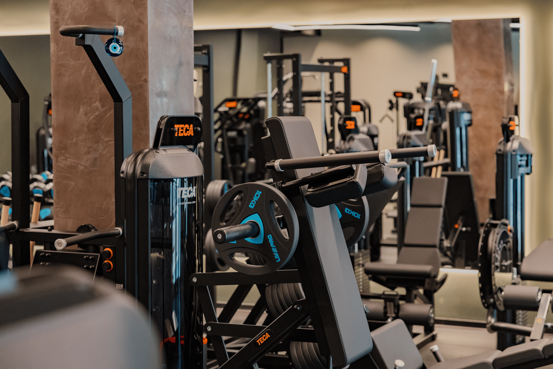 Tre persone si stanno riscaldando in una palestra con pavimento nero e grandi finestre, preparandosi per un allenamento.