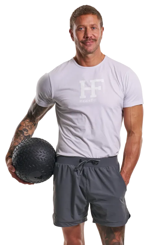 Man in gray workout clothes holding a black medicine ball, standing against a white background