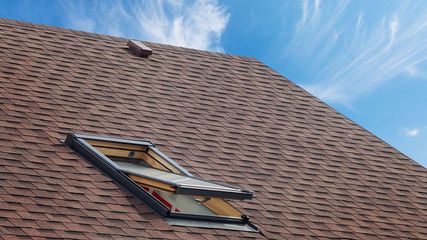 Open skylight on a brown shingled roof under a blue sky