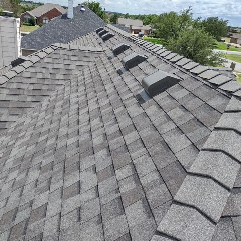 Gray shingled roof with several black skylights, viewed from above in a suburban neighborhood