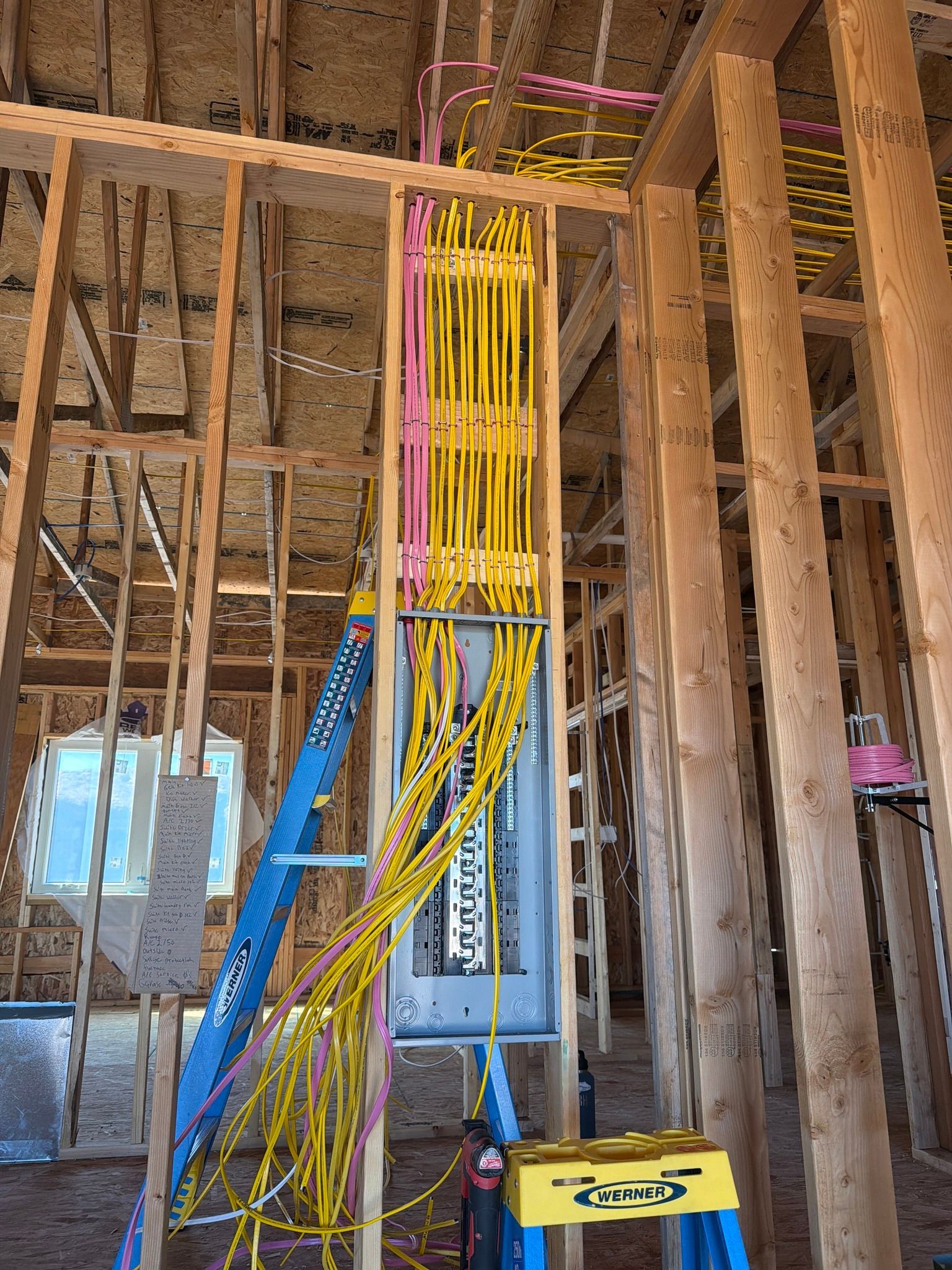 Construction site interior with exposed wooden framing, blue ladder, and bundled yellow electrical wires hanging down
