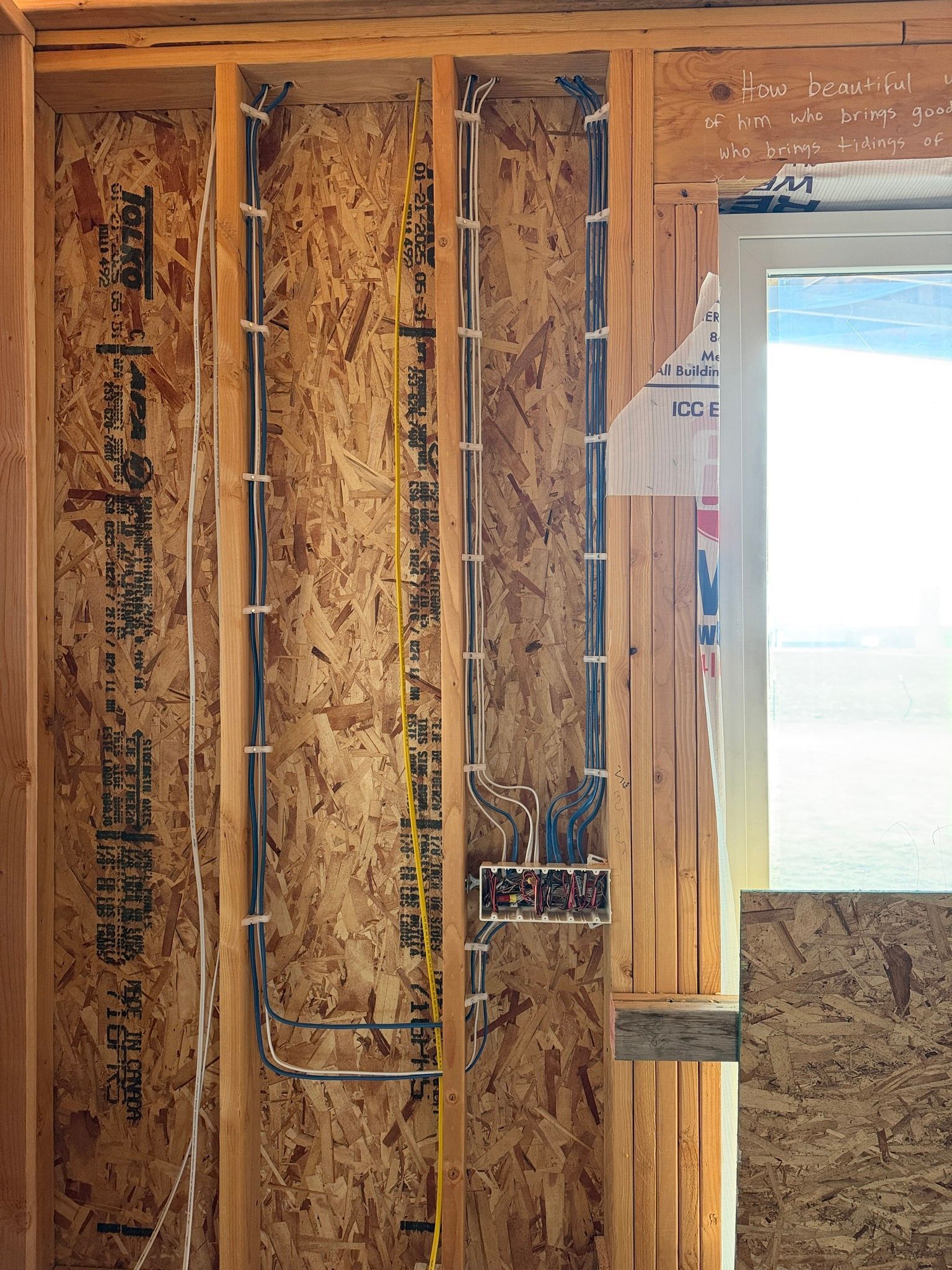 Unfinished wall framing with exposed insulation and wiring beside a bright window opening