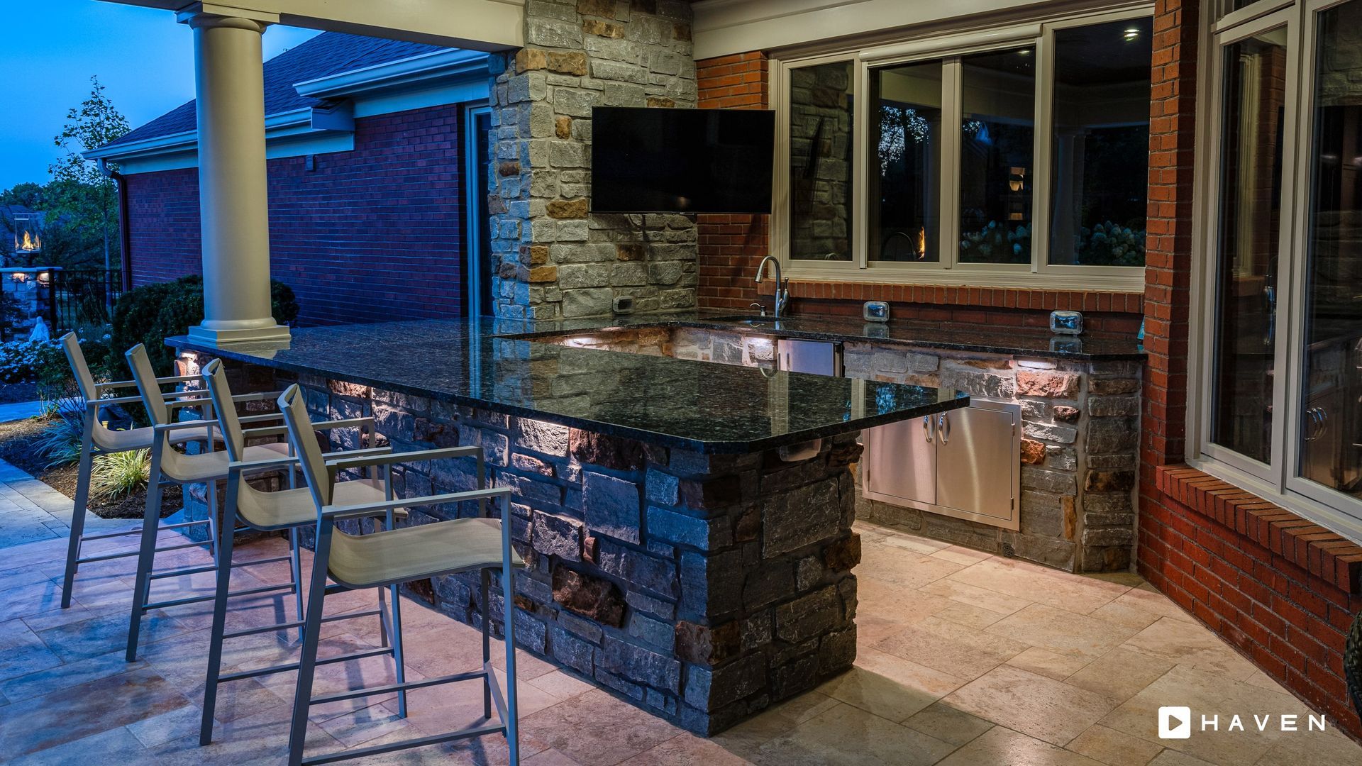 A patio with a large table and chairs and a television on the wall.