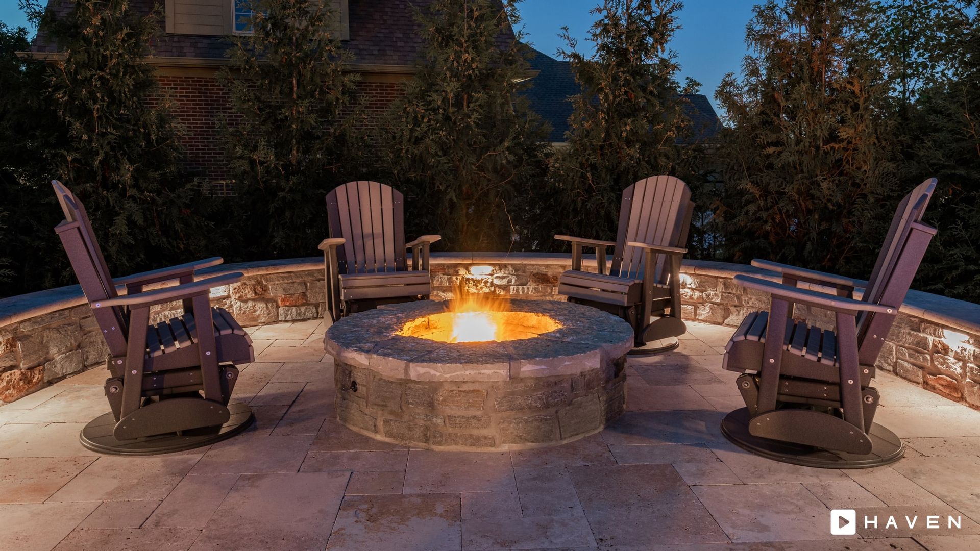 A fire pit is surrounded by chairs on a patio at night.