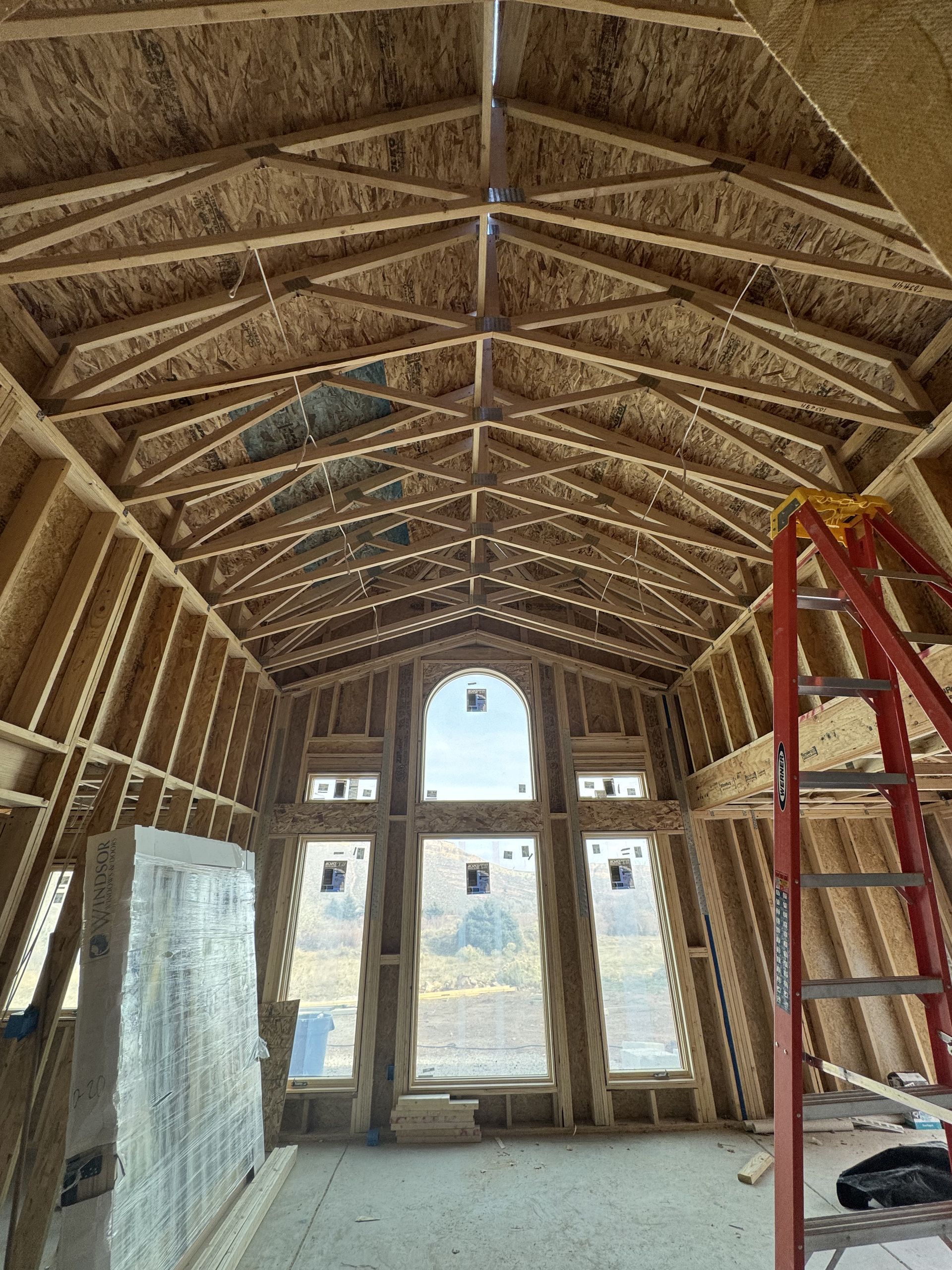 Interior view of a building under construction, featuring wooden framing, arched ceiling, and large windows.