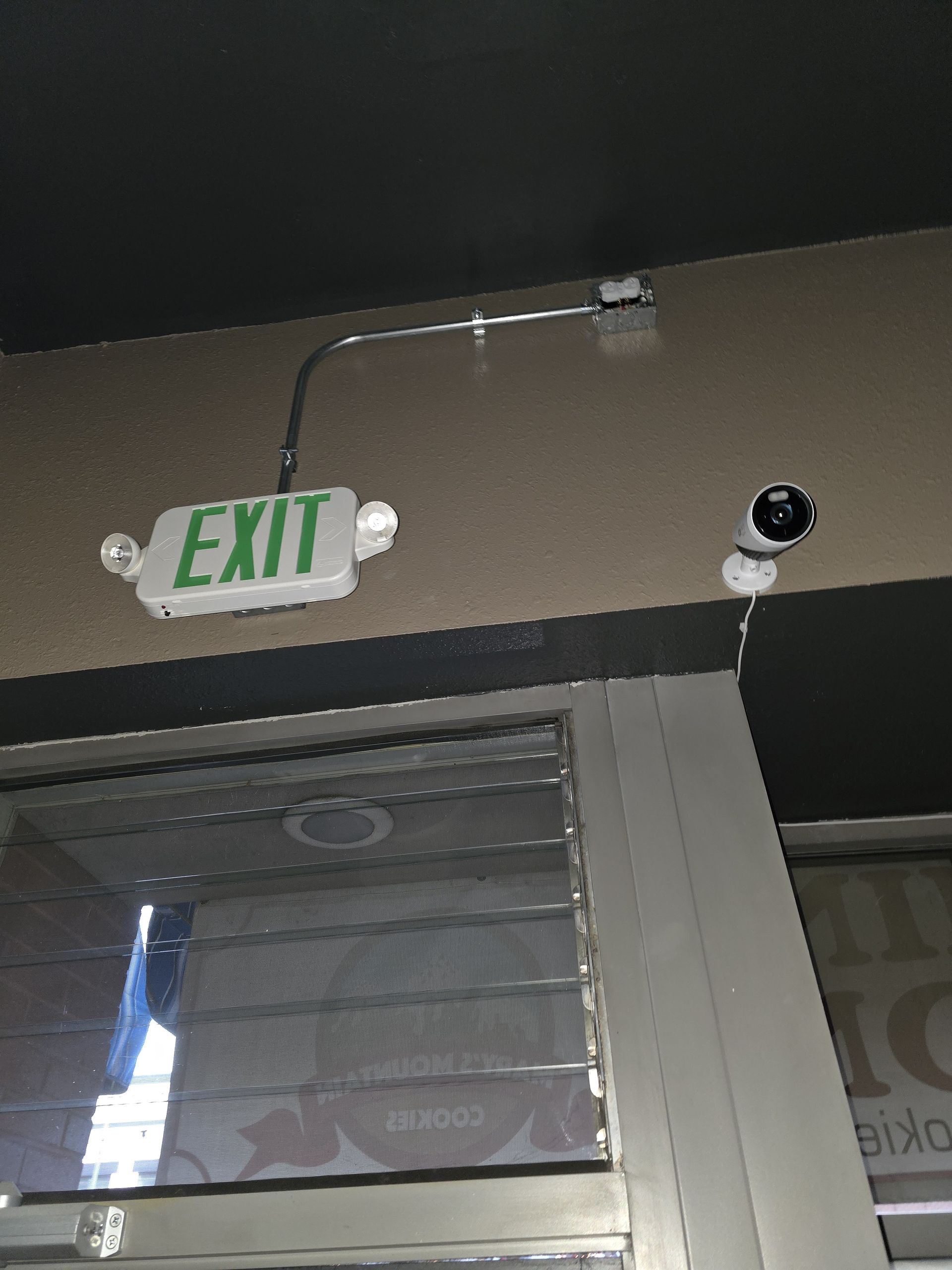 An exit sign and security camera above a storefront window.