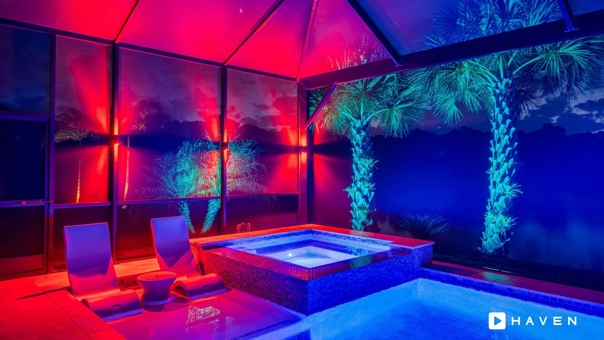 A swimming pool with a hot tub surrounded by colorful lights at night.