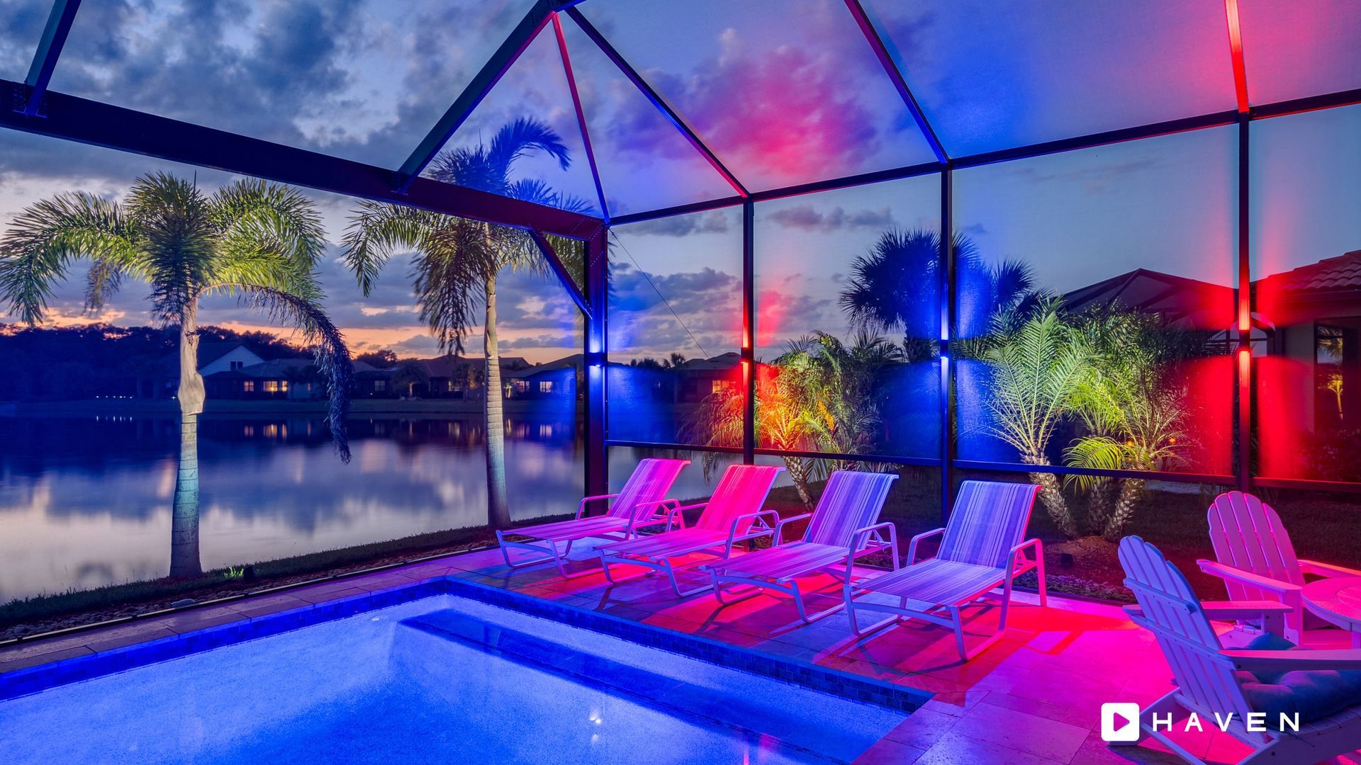 A swimming pool with chairs and a view of a lake at night.