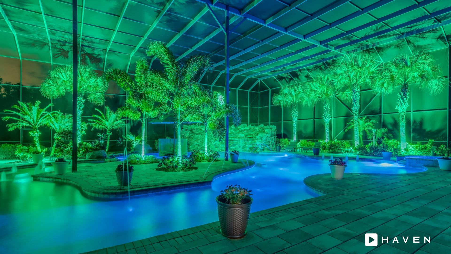 Indoor tropical oasis illuminated with blue and green lights. Palm trees surround a flowing blue stream and small islands.