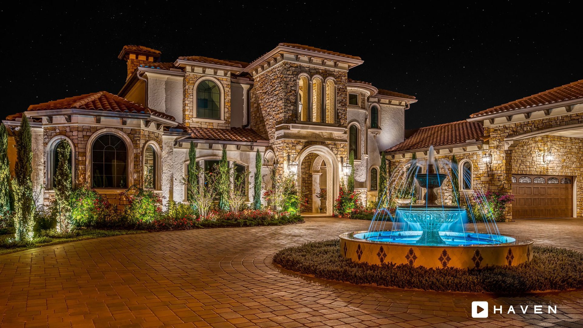 A large house with a fountain in front of it at night.