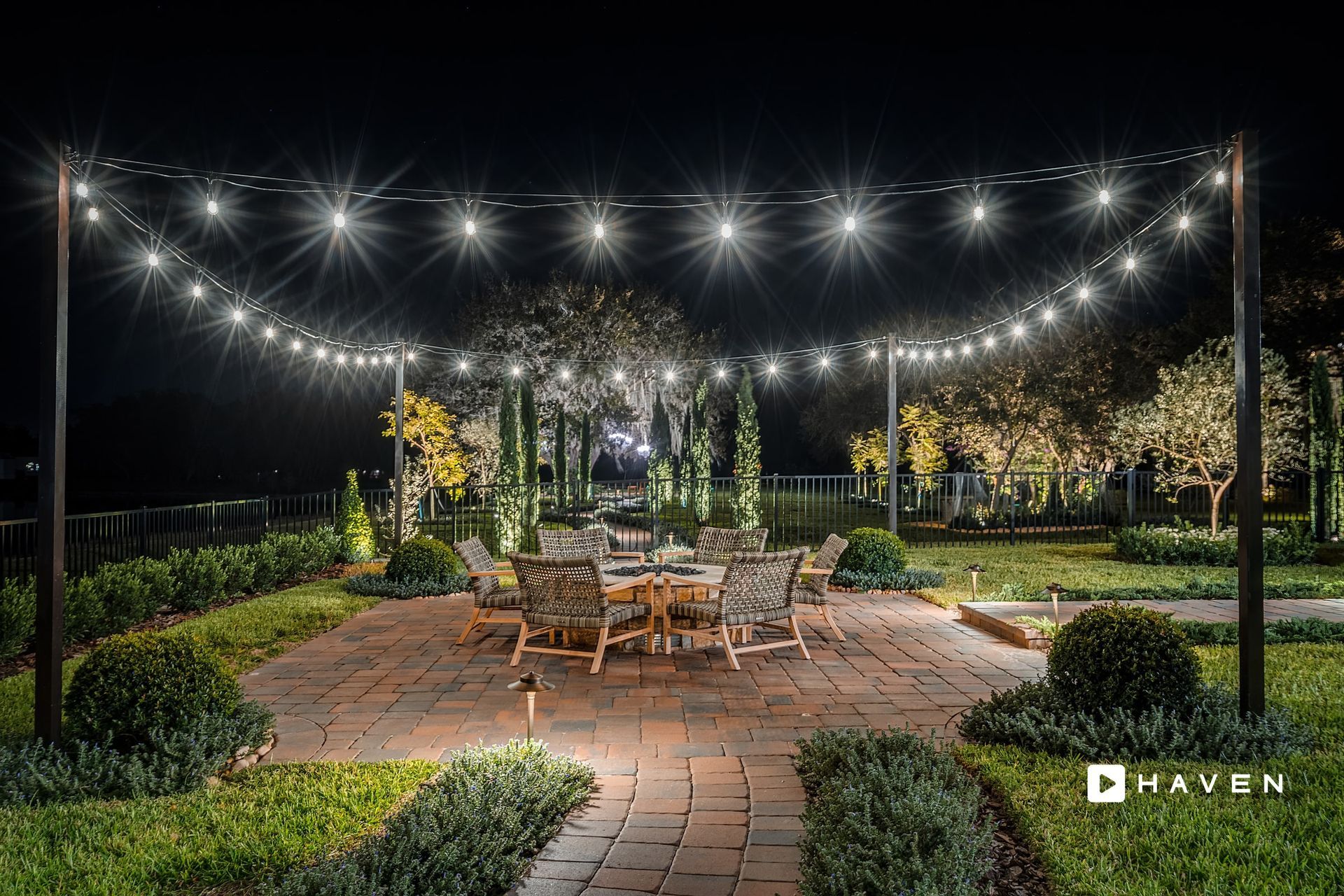 A patio with a table and chairs under a string of lights at night.