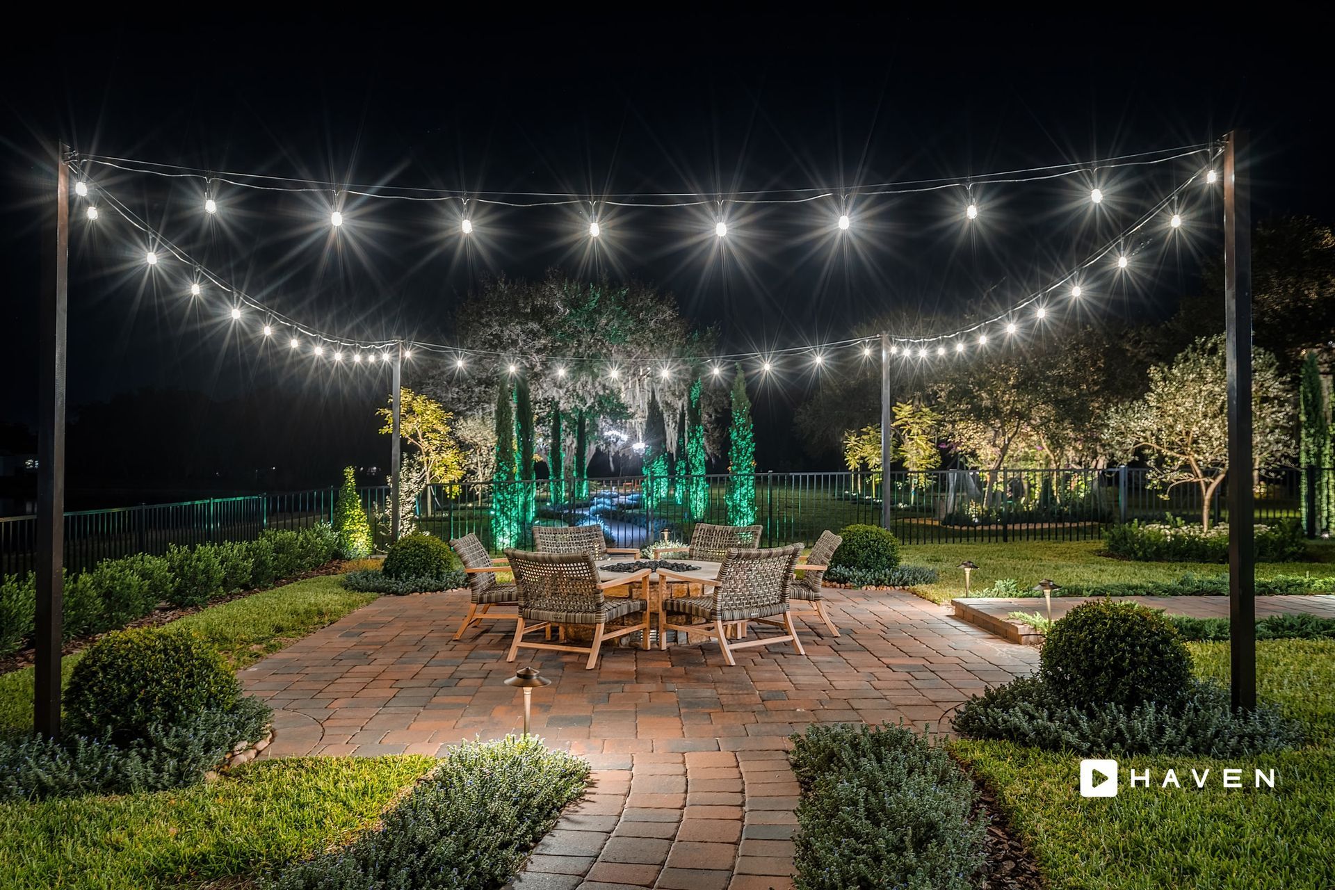 A patio with a table and chairs under a string of lights at night.