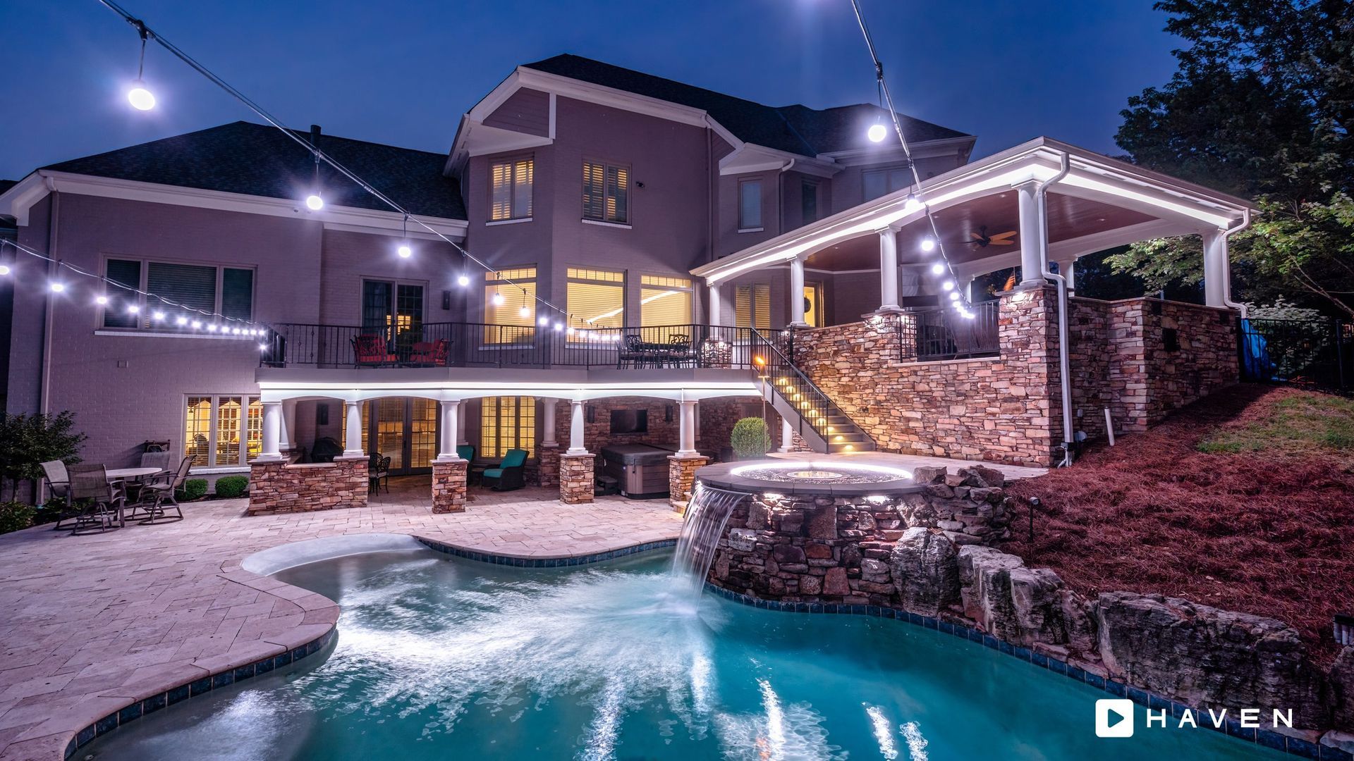 A large house with a swimming pool in front of it at night.