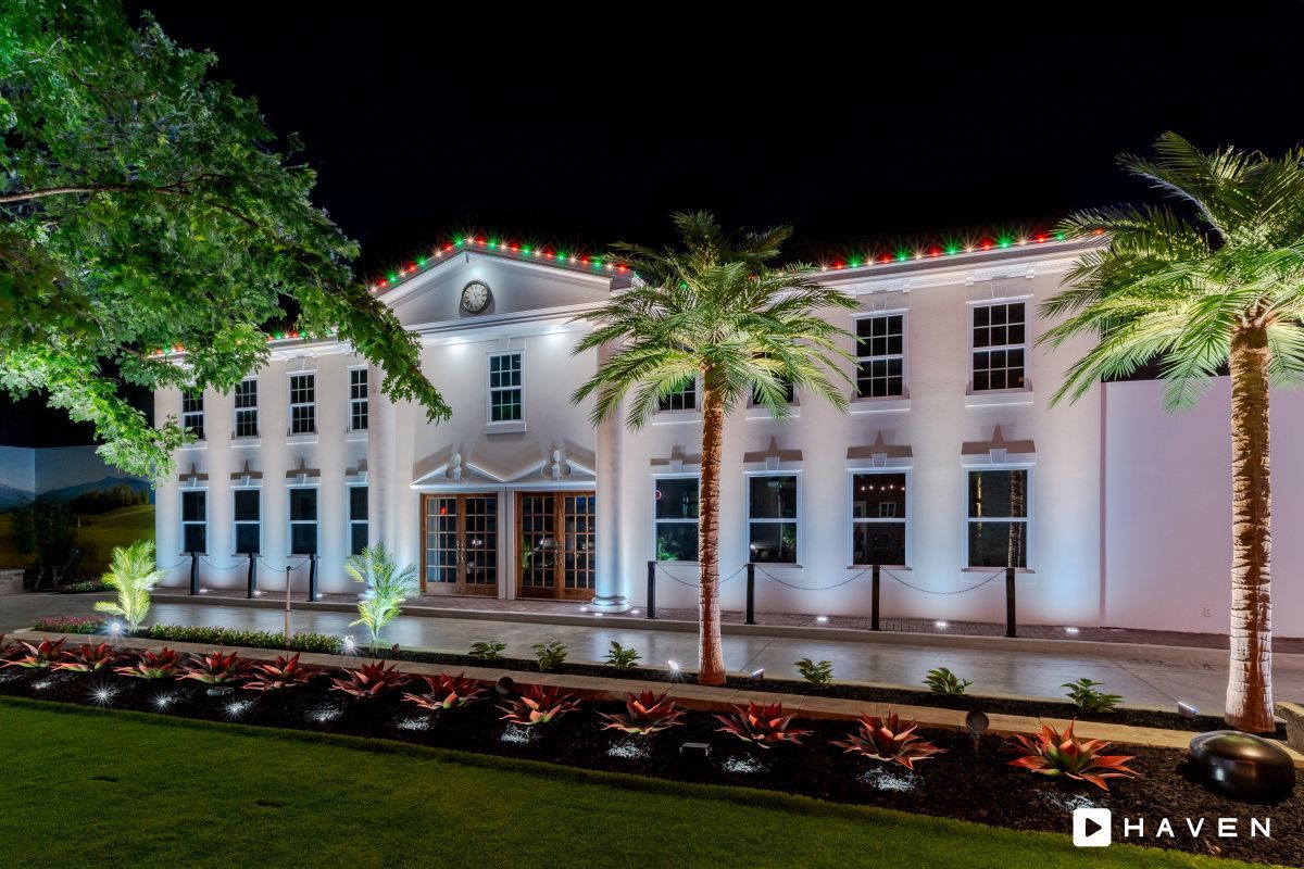 A large white building is decorated with christmas lights and palm trees.