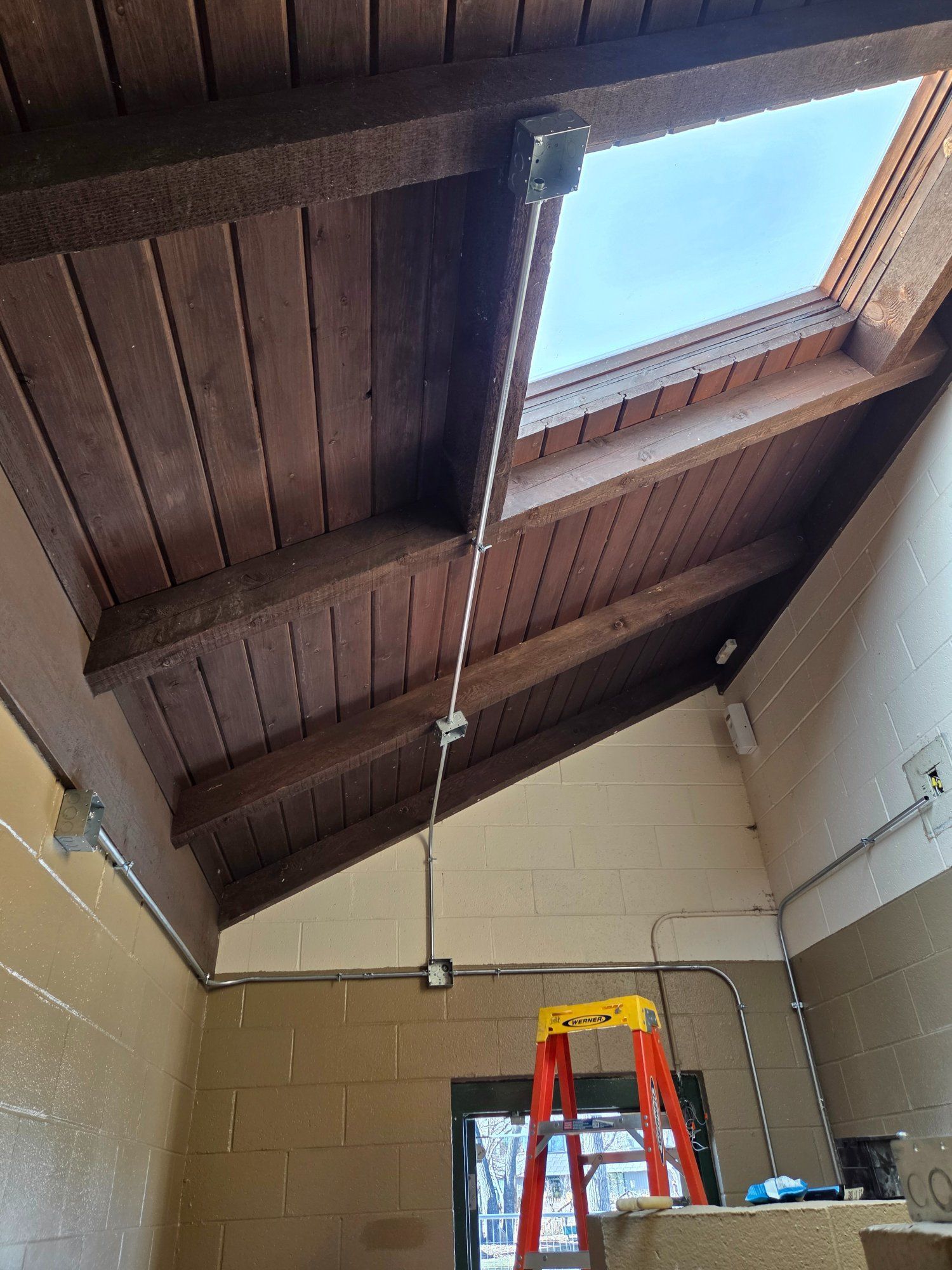 Angled ceiling with a skylight, electrical wiring, and a stepladder.