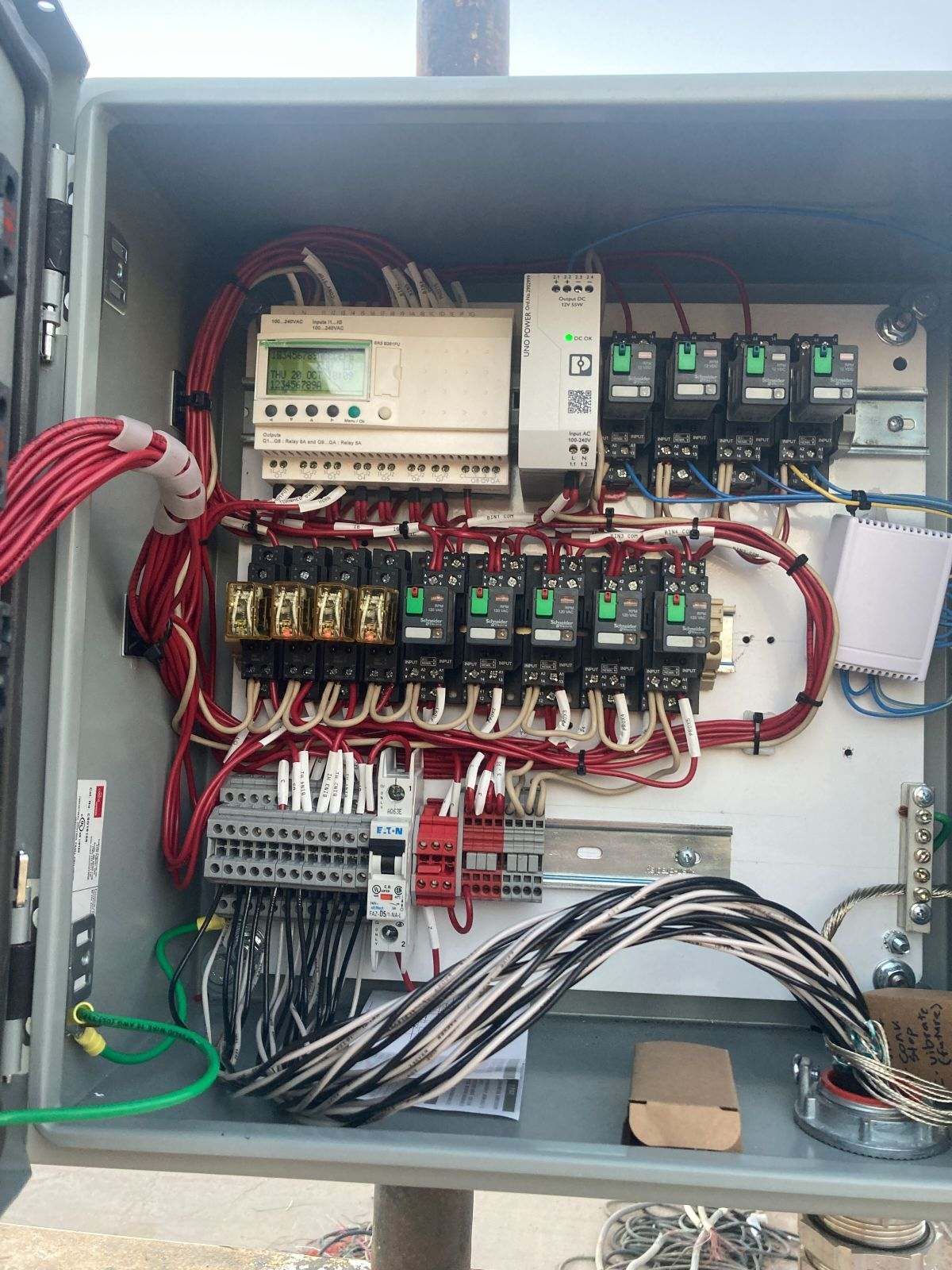 Electrical control panel with wires, breakers, and a controller inside a gray metal box.