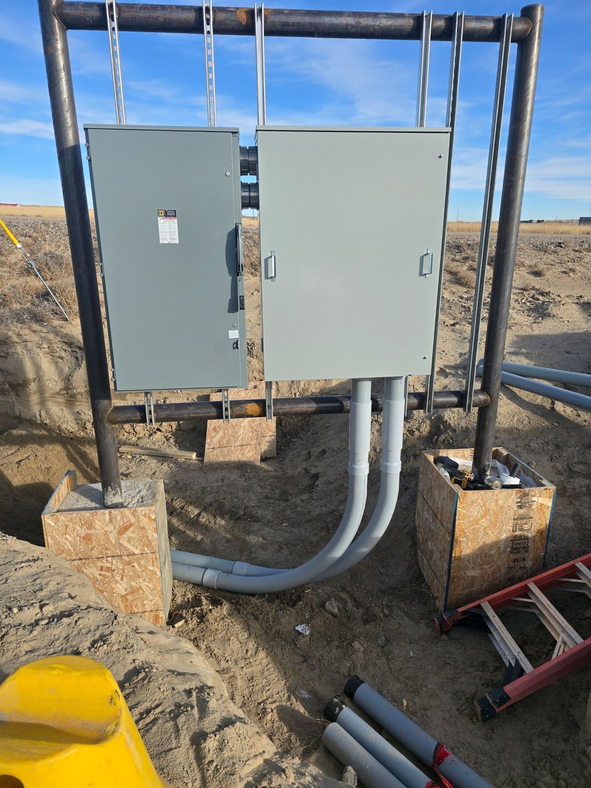 Electrical boxes mounted on a steel frame, with conduit running underground in an outdoor setting.