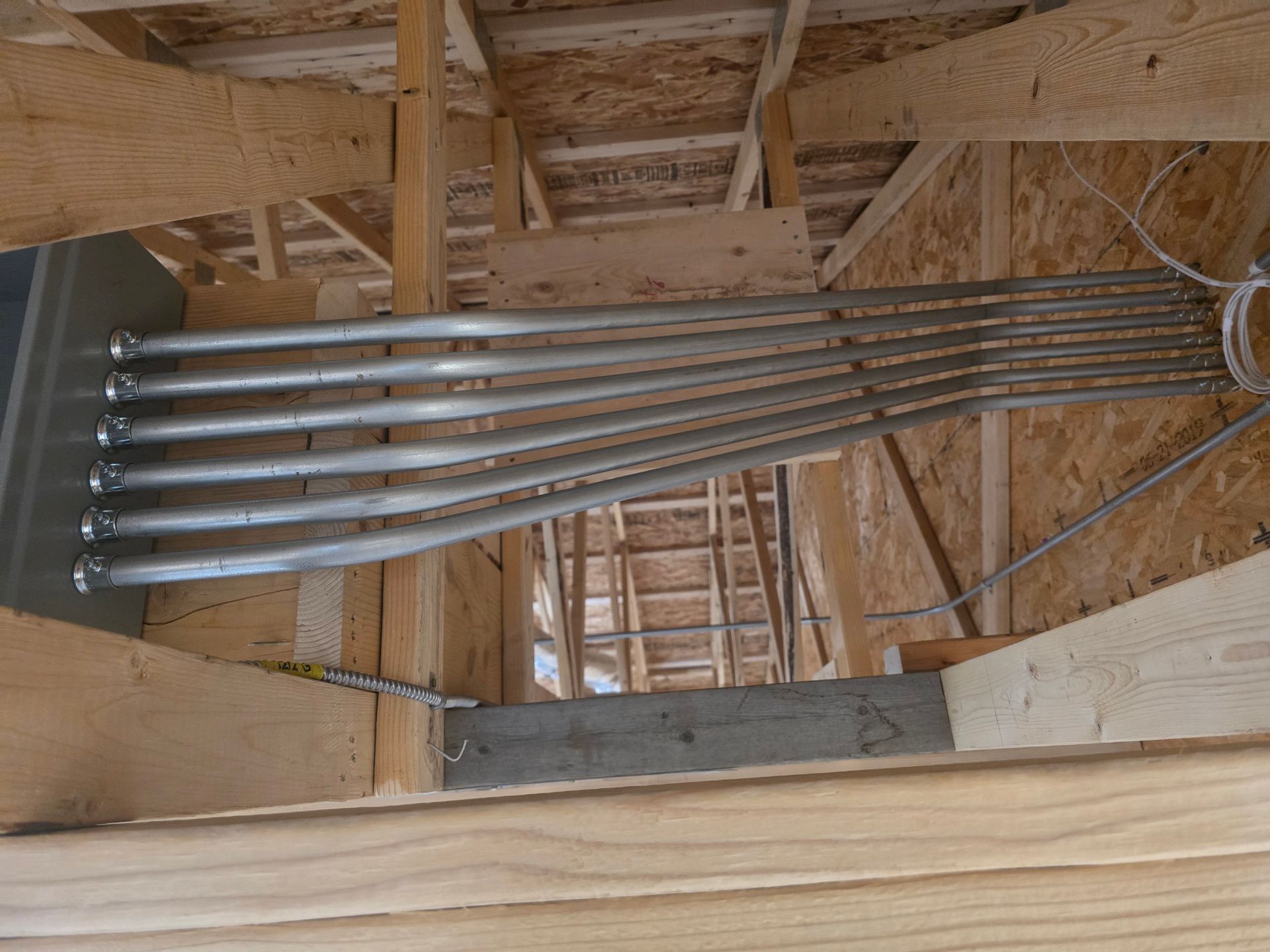 Electrical conduits run through wooden rafters in a building under construction.