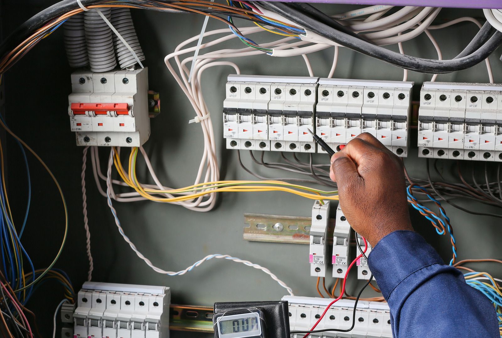 Electrician working inside an electrical panel, adjusting wiring and circuit breakers.