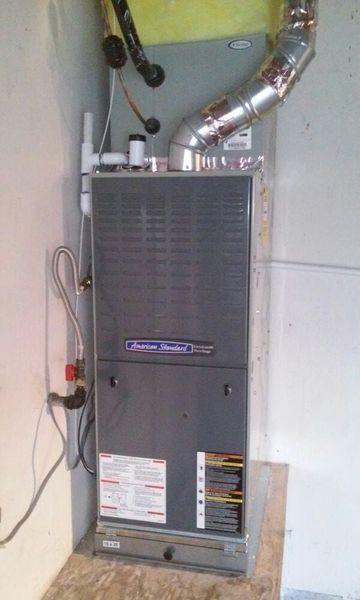 Furnace in a utility room. Gray metal unit with vents and pipes, against neutral walls.